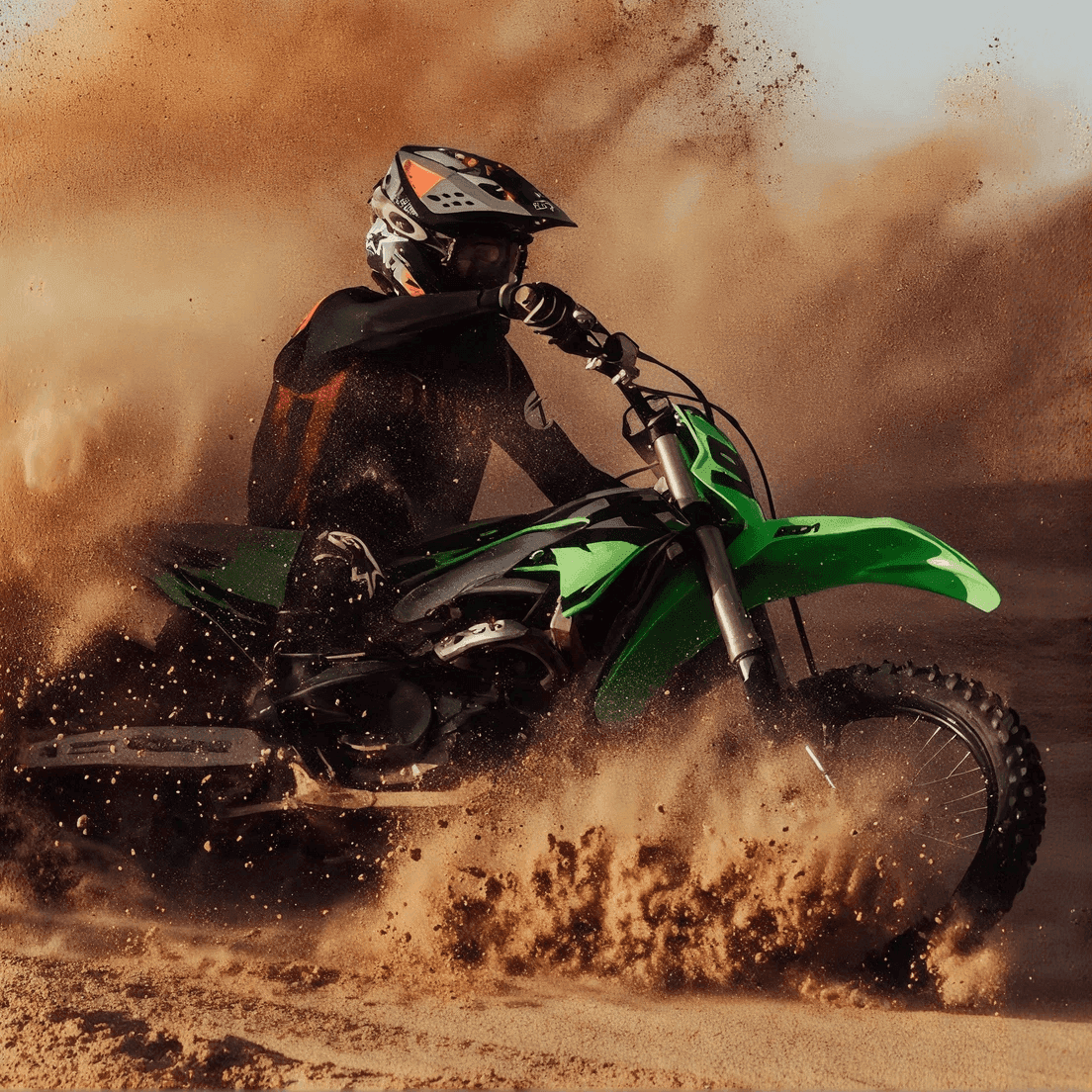 Motocrossförare som sparkar upp sand och damm på en grön terrängmotorcykel i en Sharp-kurva.